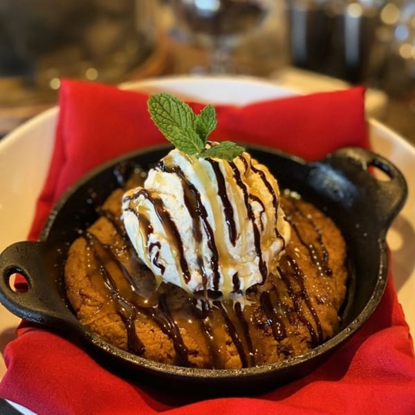 A skillet cookie with vanilla ice cream, chocolate, and caramel drizzle, garnished with mint.