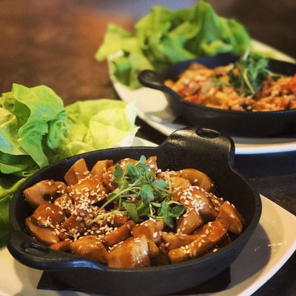 Two cast iron bowls of lettuce wraps, one with mushrooms and sesame seeds, the other with chicken.