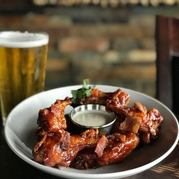 A plate of The Hive's sticky BBQ wings with dipping sauce and a glass of beer.