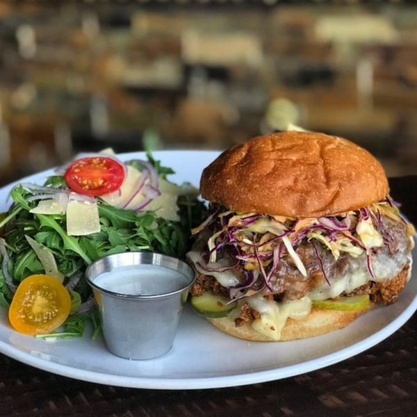 The Hive's fried chicken sandwich with melted cheese, coleslaw, pickles, and a side salad.