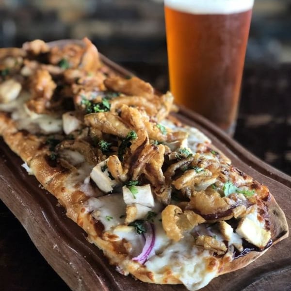 The Hive's flatbread pizza with fried onions, mushrooms, and cheese, served with a glass of beer.