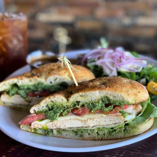 A chicken pesto sandwich on focaccia bread with a side salad and iced tea at The Hive.